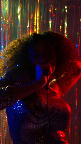 Vertical-Video-Of-Young-Woman-With-Microphone-Singing-At-Karaoke-Nightclub-Bar-Or-Disco-With-Sparkling-Lights-In-Background
